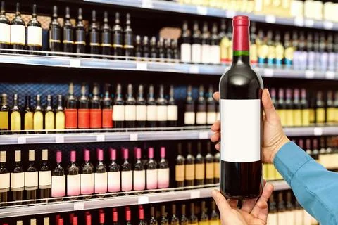 Wine bottle with empty label in man's hands in front of wine bottles on shelv Stock Photos