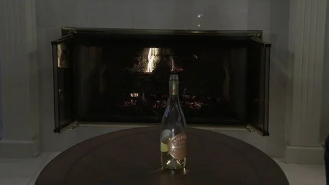 Wine bottle in front of fireplace as hands take up wine glasses, 4K. Stock Footage 84790822
