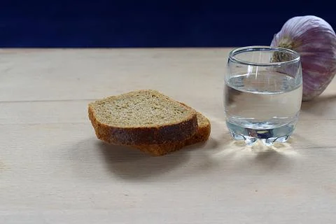 Wine-glass of vodka, bread and garlic on a wooden table. Stock Photos