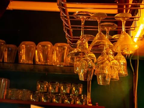 Wine glasses hanging upside down on rack above bar shelf with warm golden a.. Stock Photos
