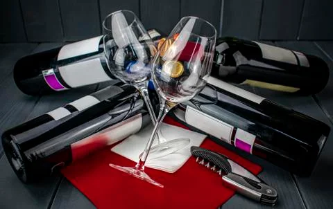 Wine glasses lying on several bottles of red wine and a corkscrew, on red tab Stock Photos
