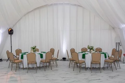 Wine glasses, silver tableware and green napkins on round tables covered wi.. Photos