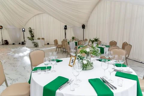 Wine glasses, silver tableware and green napkins on round tables covered with Stock Photos