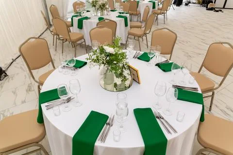 Wine glasses, silver tableware and green napkins on round tables covered wi.. Stock Photos