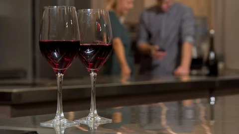 Wine glasses on the table, couple using smart phone together at home on the back Stock Footage 102897586