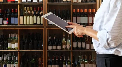 Wine shop manager using computer tablet while working at store. Stock Photos