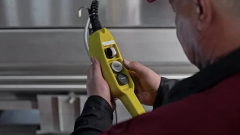 Wine worker in uniform presses a button on the remote control of a machine. Stock Footage 268750355