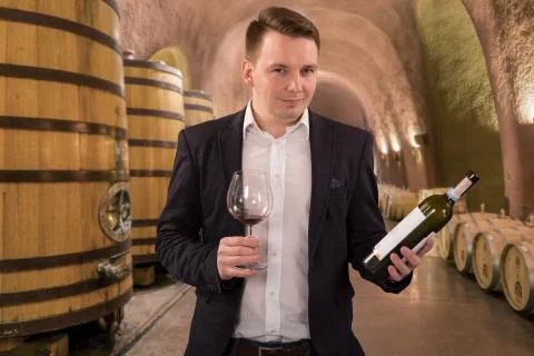Winemaker inspecting quality of red wine, standing near bottles racks in wine Stock Photos