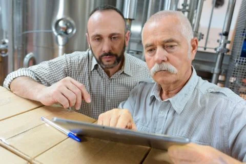 Winemakers in cellar using electronic tablet to control wine quality Stock Photos
