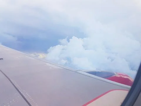 Wing of aircraft with red engine and silver surface cutting through a cloudy  Stock Photos