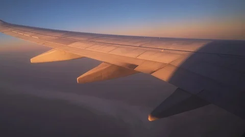 Wing of an airplane flying above the clouds at sunrise Stock Footage 121618102