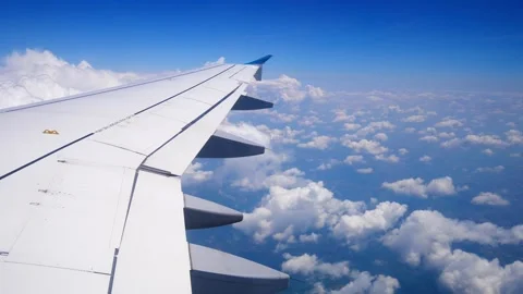Wing of an airplane flying above the clouds on blue sky. View from a window of Stock Footage 246831144
