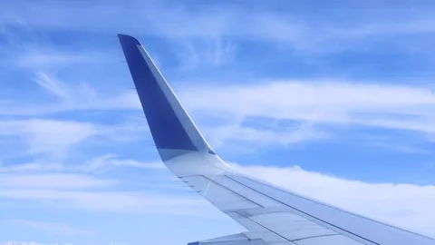 Wing of an airplane flying above the clouds on blue sky Stock Footage 248497373
