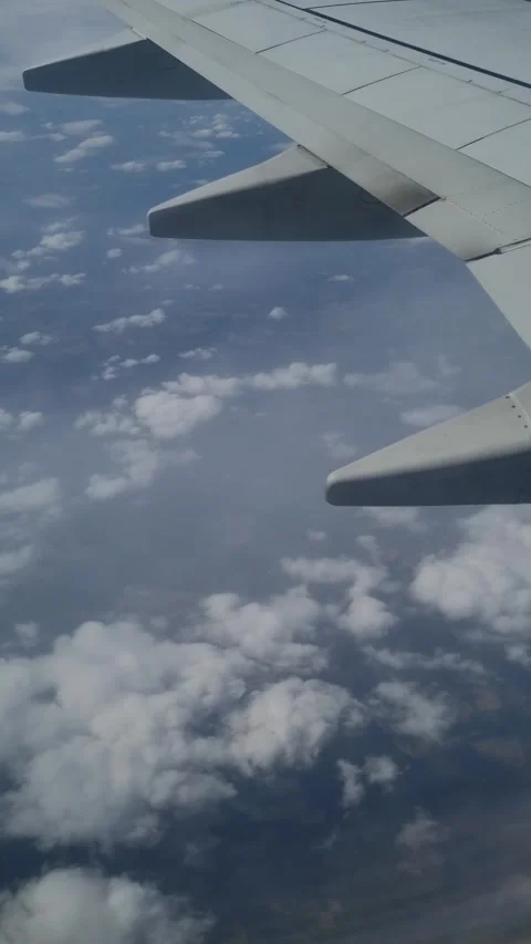 Wing of an airplane flying above the clouds on blue sky. View from a window  Stock Footage 277678901