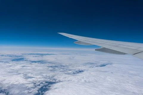 Wing of a flying plane over clouds on the blue sky. Stock Photos