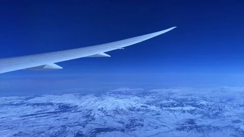 Wing of a passenger aircraft in front of a dark blue sky with tall mountains. Video stock 201459282