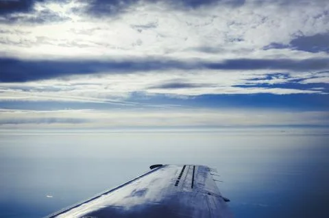 The wing of the plane in a cloudy sky, sun behind the clouds Stock Photos