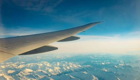 Wing of plane over mountain cover with white snow. Airplane flying on blue sk Stock-Fotos
