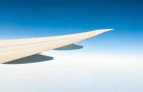 Wing of plane over white clouds. Airplane flying on clear blue sky. Scenic vi 库存照片
