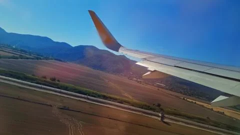 Wing of plane taking off over sunlit runway and valley, faint light with warm Stock-Fotos