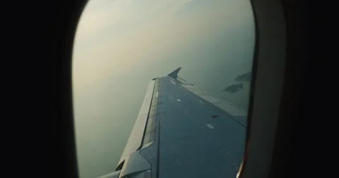 Wing visible through airplane window under soft morning light, wing reflecting Stock Footage 312122139
