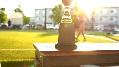Winner gold trophy with sunlight shining and athlete walking in background, 4K Stock Footage 107428298