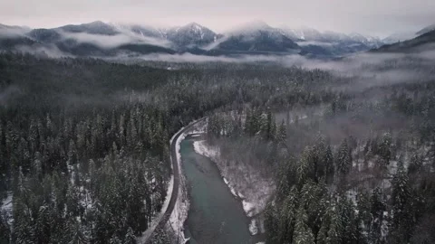 Winter Aerial River Winding Through Snowy Pine Forest and Misty Mountains Stock Footage 337756540