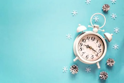Winter alarm clock with pine cone and copy space on blue background. Time to  Stock Photos