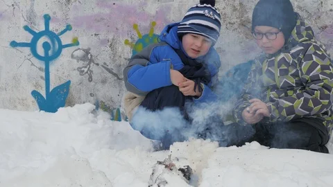 Winter bonfire smoke. Winter fire. Two small boys sit squatting and watch the Stock Footage 88184304