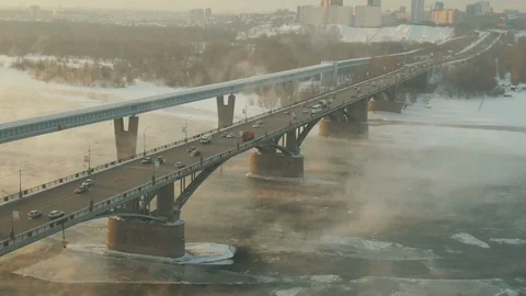 In a winter city, an impressive bridge rises above an ice-covered steamy river. Stock Footage 113751325