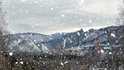 Winter cityscape on the background of mountains, falling snow Video stock 120439564