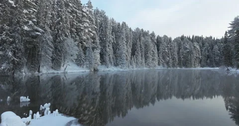 Winter cold river. Islands of snow on calm water. Forest surrounds the lake Video stock 230263405