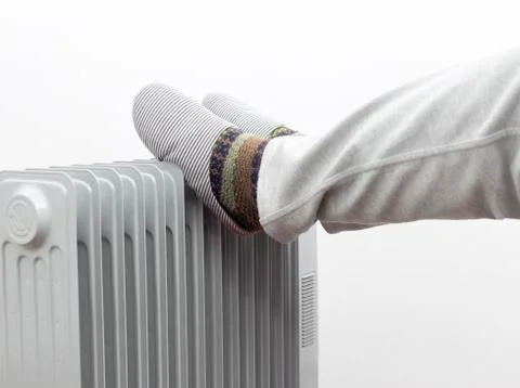 Winter concept. Unknown man placed his feet on a heater. Stock Photos