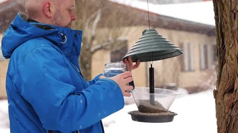 Winter day and snowfall, man fills a bird feeder Stock Footage 60696272