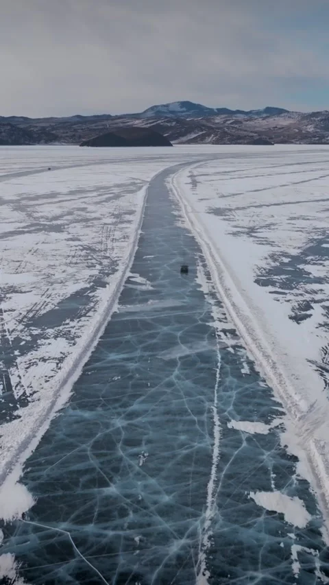 Winter drone view of Lake Baikal ice highway with deep cracks and Siberian peaks Stock Footage 346556995