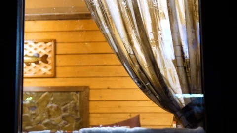 Winter evening. In a warm and bright room near the window stands a young man 動画素材 98989743