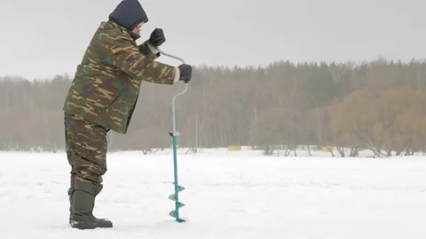 Winter fishing on river. A man drills a hole in ice Stock Footage 71961053