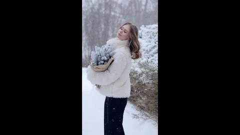 Winter forest scene featuring smiling woman in white fur coat and black pants Stock Photos