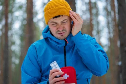 Winter hiker wincing from headache, pulling pain medication from first aid kit Stock Photos