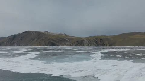 Winter ice patterns on Lake Baikal with mountain shoreline, Siberia aerial view Stock Footage 336294874