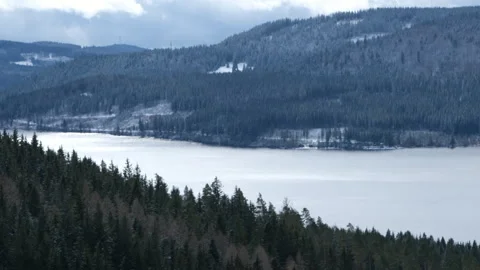 The winter lake between the mountains covered with snowy forest Stock Footage 266654343