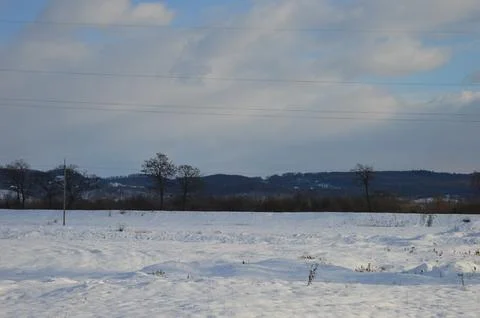 Winter landscape with snow-covered fields and distant mountains under a cloudy Stock Photos