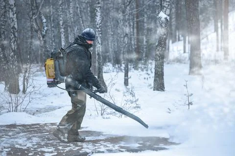 A Winter Maintenance Worker uses a Leaf Blower to clear snow in a forest, w.. Stock Photos