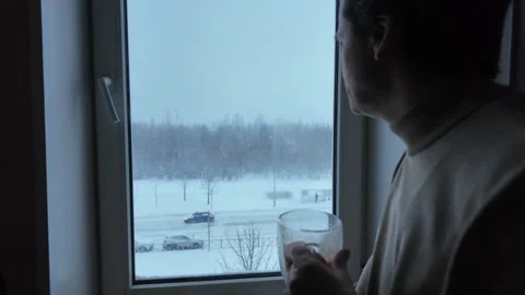 Winter. A man drinks tea looking out the window. Vídeos de archivo 331425769