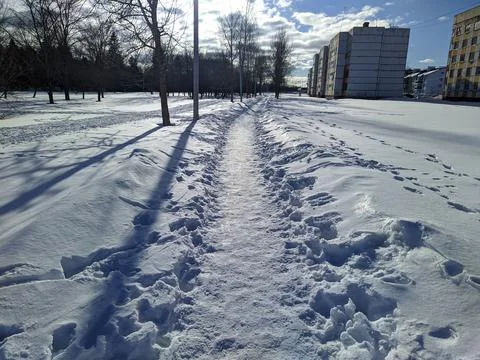 Winter path in the city behind multi-storey buildings in the sunny daytime. Stock Photos