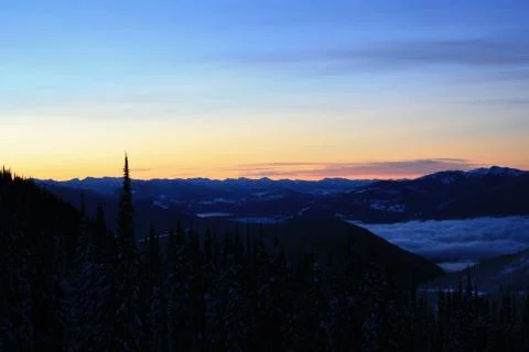 A winter photo looking down into a clouded, snow covered, forested valley Stock-Fotos