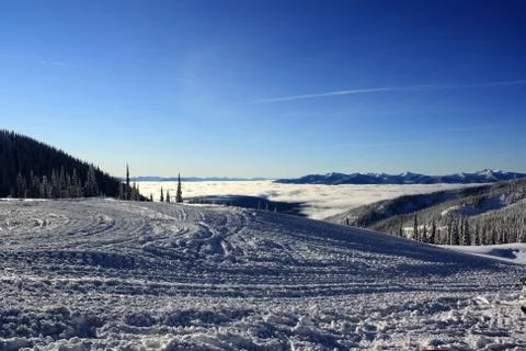 A winter photo looking down into a clouded, snow covered, forested valley Stock Photos