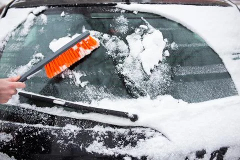 Winter problems with the car. A man cleans the car from snow with a brush Фото