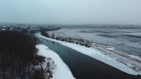 Winter river flows beside snowy fields in rural area during overcast weather Stock Footage 329707852