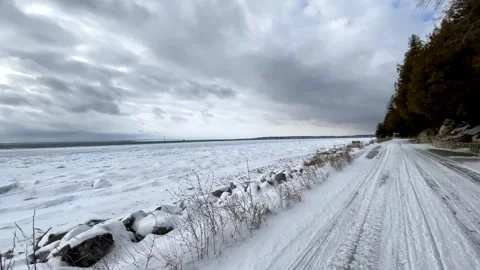 Winter road alongside a completely frozen lake with thick ice and cloudy sky Stock Footage 325477707